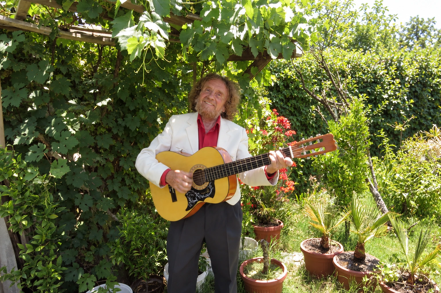 Axel Pinto-Agüero sin sombrero, con su guitarra bajo una parra